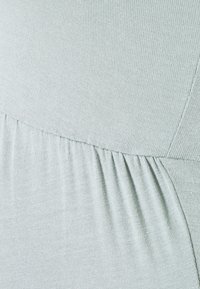 Vaaleanvihreä, teksturoitu kangas, jossa on poimutettuja ja uurrettuja yksityiskohtia, sileä viimeistely ja virtaava muotoilu lisämukavuutta ja liikkuvuutta varten.