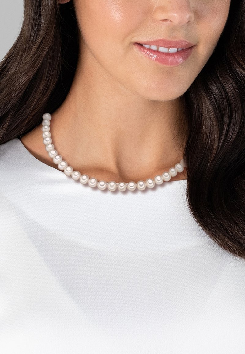Pearl necklace featuring round, lustrous white pearls strung together, resting along the collarbone, above a plain white garment.