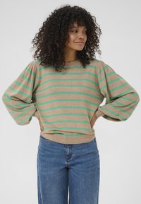 Maglione beige con stripe orizzontali verdi, scollatura tonda e maniche a sbuffo. Abbinato a jeans a gamba larga blu. Tessuto morbido.