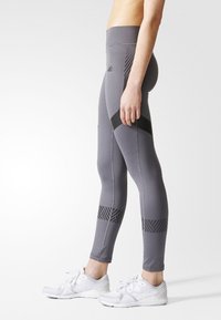 Šedé sportovní legíny s vysokým pasem, zdobené kontrastními černými akcenty a geometrickým vzorem na spodní části nohavic.