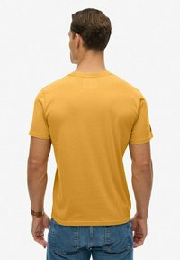 Camiseta amarilla mostaza de algodón, con un clásico cuello redondo y mangas cortas, con una textura suave y lisa.