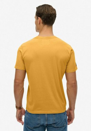 Camiseta amarilla mostaza de algodón, con un clásico cuello redondo y mangas cortas, con una textura suave y lisa.