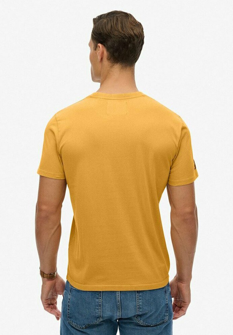 Camiseta amarilla mostaza de algodón, con un clásico cuello redondo y mangas cortas, con una textura suave y lisa.