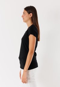 T-shirt nera a maniche corte con collo rotondo, realizzata in tessuto liscio, design aderente, indossata con pantaloni bianchi.