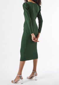 Vihreä ribbikuvioinen midi-mekko, jossa on pitkät hihat ja kootut olkapäät, yhdistettynä hopeisiin lohkotossuihin, joissa on hihnadesign.