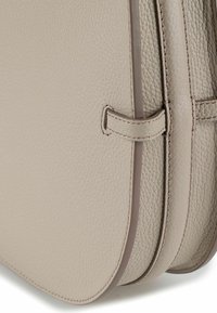 Beige leren handtas met een gestructureerde afwerking, gebogen vorm, subtiele stiksels en een dunne contrasterende rand langs de randen.