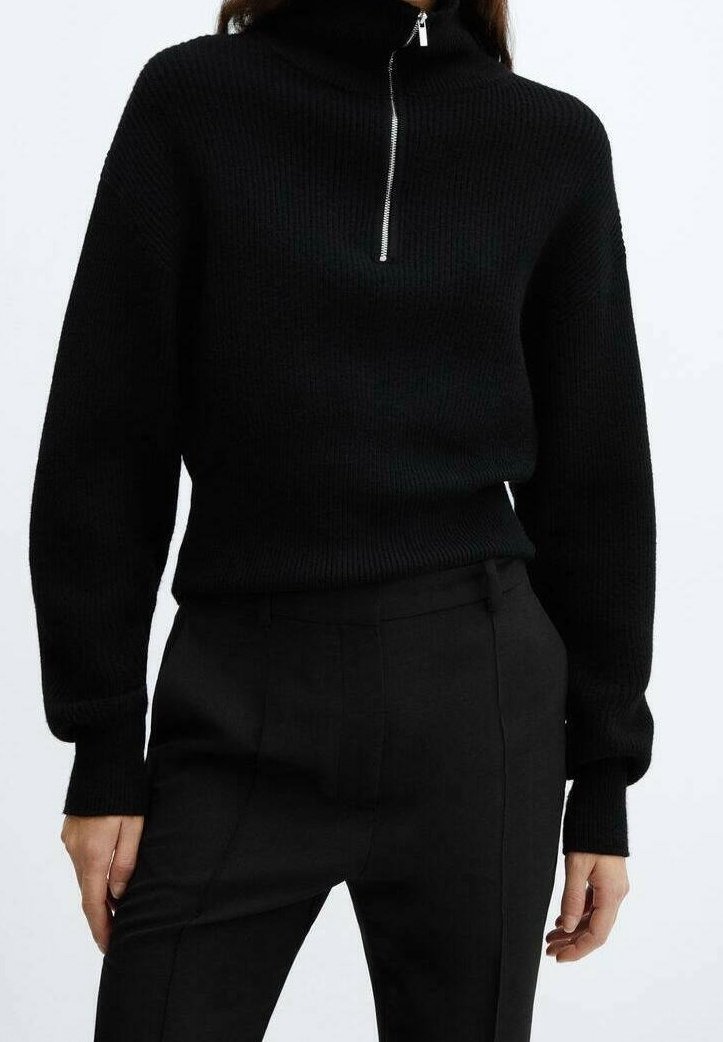 Sort ribstrikket sweater med høj krave og kort lynlås, kombineret med sorte, skræddersyede bukser, der viser et tekstureret strikkemønster.