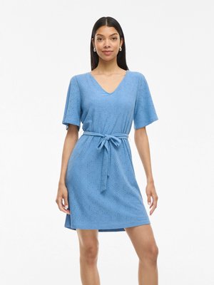 Robe courte bleu clair avec un décolleté en V, des manches courtes et une taille nouée. Le tissu présente un motif texturé en œillets.