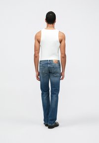 Jeans de ganga azuis com um design de perna reta, apresentando uma etiqueta nas costas. Usados com uma t-shirt branca justa e sapatos pretos.