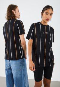 Svart kortärmad t-shirt med vertikala orange och vita ränder, med en lös passform och en diskret logotyp på bröstet.