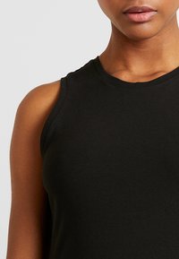 Top noir sans manches en tissu lisse et extensible, avec un décolleté rond et une coupe près du corps. Aucun motif ni matériel visible.