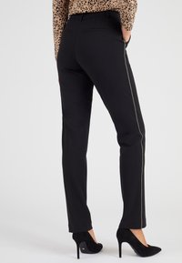 Pantalones negros ajustados con un corte slim, que presentan una sutil franja beige en el costado. Están confeccionados con una tela suave y cuentan con bolsillos traseros clásicos.