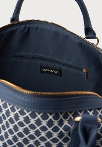 Navy színű, szintetikus anyagból készült táska geometrikus mintával. Arany tónusú cipzárral és bélésse, belső zsebbel és logós címkével rendelkezik.