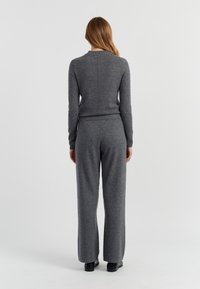 Grau gestrickter Pullover mit Rundhalsausschnitt, kombiniert mit weiten grauen Hosen, beide mit einem weichen Material und subtilen Nähten.