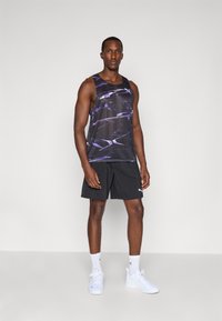 Top negro sin mangas con un patrón abstracto púrpura, acompañado de pantalones cortos negros. Modelo con zapatillas deportivas blancas y calcetines con acentos de logo.