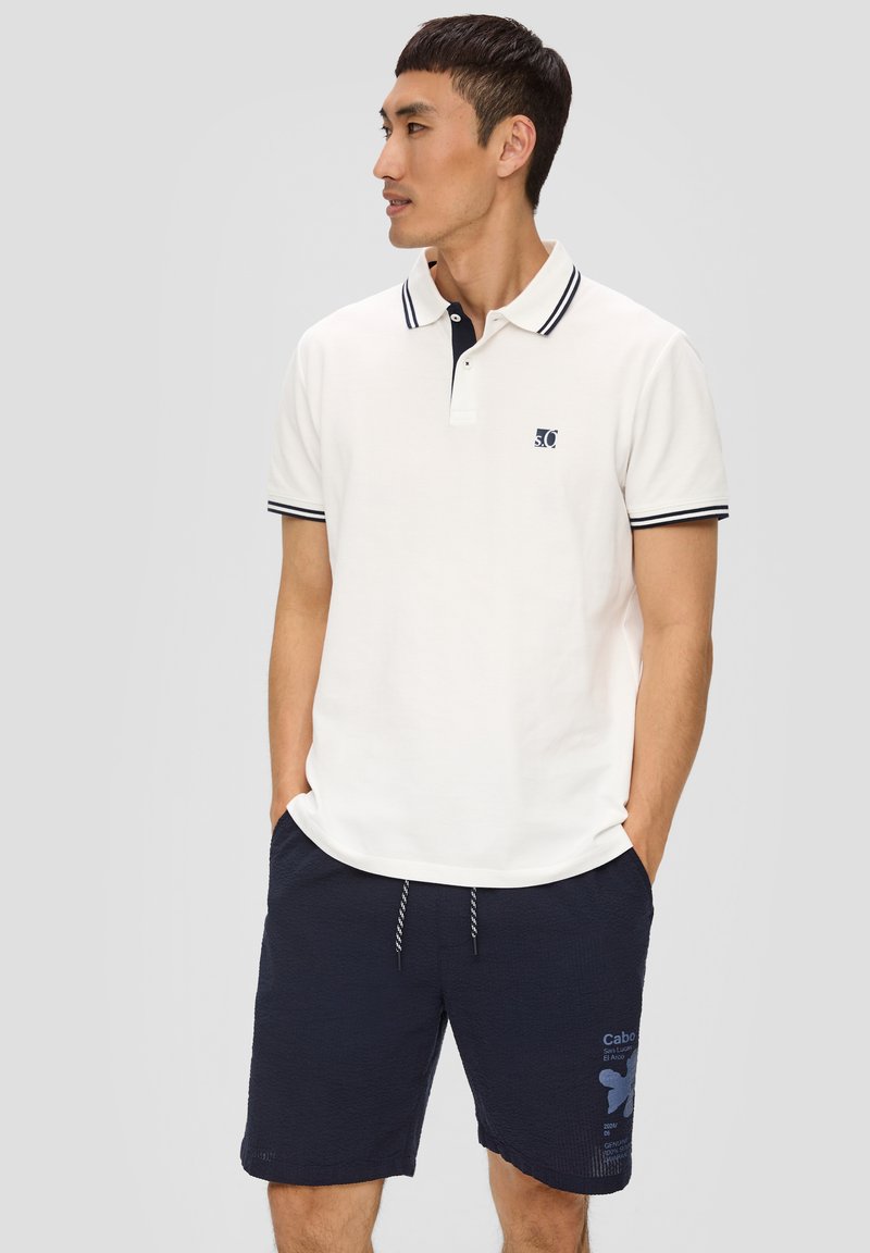 Polo à manches courtes en crème avec un col marine et des accents rayés, associé à un short marine en tissu texturé avec des détails imprimés.