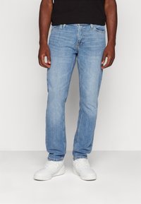 Světle modré džíny s rovným střihem, pěti kapsami a kontrastním prošíváním, spárované s bílými sportovními botami.