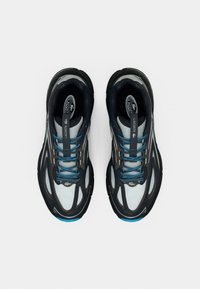 Μαύρα και γκρι αθλητικά παπούτσια με υφασμένο διχτυωτό επάνω μέρος, μπλε κορδόνια, επενδυμένη σόλα και λογότυπο Lacoste στη γλώσσα.