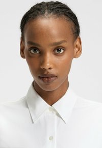 White button-up shirt with a pointed collar, made of smooth fabric, featuring a front placket with buttons. No visible patterns or accents.