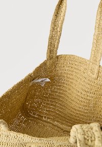 Υφαντή τσάντα χειρός από ψάθα σε κίτρινο χρώμα, με ανοιχτό σχέδιο, δύο γερά χερούλια και υφασμένο εσωτερικό με ορατές ετικέτες φροντίδας.