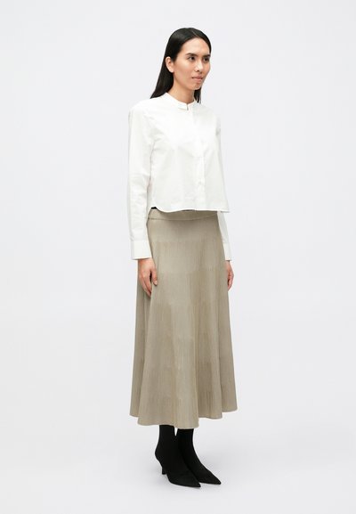 Λευκό cropped πουκάμισο  με κουμπιά και μανταρίνι γιακά, συνδυασμένο με μπεζ πλισέ midi φούστα και μαύρες γόβες με μυτερή μύτη.
