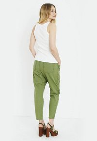Haut sans manches blanc associé à un pantalon olive décontracté avec des poches arrières, et des sandales à talons hauts marron.