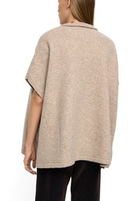 Beżowy, oversize sweter z miękkiej dzianiny, z przewracanym kołnierzem, opadającymi ramionami i surowym wykończeniem na dole.