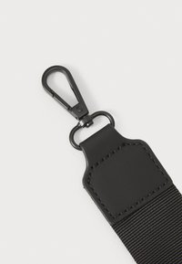 Zwarte nylon strap met een metalen clip en ring. Beschikt over een gestructureerd oppervlak en gestikte accenten op een plastic connector.