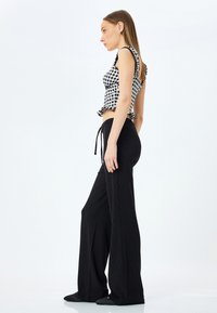 Zwarte wijde broek gecombineerd met een geruit crop top met ruffles aan de mouwen. De top heeft een getailleerd ontwerp, terwijl de broek een gestructureerde afwerking heeft.