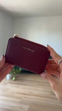 Burgundowa skórzana portmonetka z zamkiem błyskawicznym, teksturowana powierzchnia i złote logo. Kompaktowy design ułatwiaj�ący obsługę i przechowywanie.