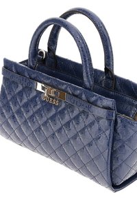Sac à main matelassé bleu marine avec deux poignées courtes, matériel métallique et un logo proéminent. Texture lisse et forme structurée.