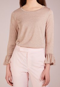 Haut rose clair à manches longues avec une texture scintillante et un col rond, avec des poignets volantés et une coupe décontractée, assorti à un pantalon coordonné.