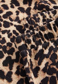 Tessuto animalier a macchie di leopardo in beige e nero, con una texture rigata e un dettaglio elastico arricciato lungo il bordo.