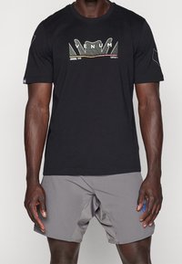 Camiseta negra de manga corta con el logo de VENUM que presenta acentos multicolores. Combinada con pantalones cortos grises, mostrando una tela de algodón ligera.