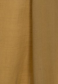 Textil en un cálido tono dorado, con una textura suave y tejida, adornada con un sutil patrón diagonal. La tela cae con suavidad.