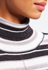 Raidoitettu pooloneule tummanharmaana, valkoisena, vaaleanpunaisena ja hopeanvärisenä. Neuleessa on resorimainen rakenne ja kimalteleva lanka. Lähikuva kaula-aukosta.