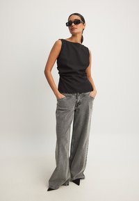 Must musta top, millel on kitsas lõige, koos laia säärega hallide teksade ja mustade teravatipuliste kontsakingadega. Tumedad prillid lisavad välimusele viimast viimistlust.