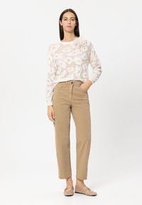 Light pink sweater with white abstract pattern, beige cotton pants, and woven flat shoes. The sweater features a textured floral accent.