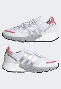 Zapatillas deportivas blancas con parte superior de malla, detalles plateados, talón rosa y una suela texturizada con una entresuela gruesa de espuma.