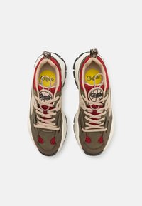 Scarpe da ginnastica con pannelli verde oliva e beige, accenti in rete rossa, lacci crema e suola in gomma nera, con un logo circolare sulla linguetta.