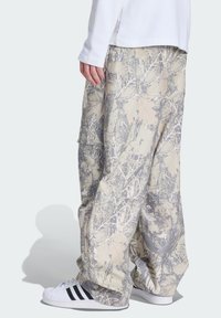 Camouflage cargobukser i beige og grå, med en løs pasform, flere lommer og indviklede bladmønstre. Kombineret med sorte og hvide sneakers.