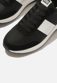 Zwarte sportieve schoenen met een mix van glad textiel en suède materialen, met zwarte veters en een witte accentstreep aan de zijkant.