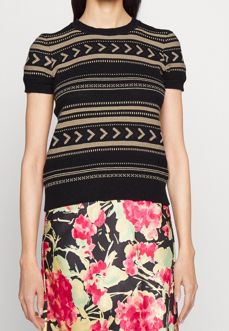 Stickad kortärmad tröja i svart och beige med geometriska mönster. Figursydd design och rund halsringning, kombinerad med en blommig mönstrad kjol.