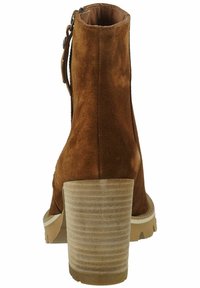 Bota de tobillo de ante marrón con un cañón cónico, tacón acanalado en tono beige y cremallera lateral. Cuenta con una suela de goma plana y punta redondeada.