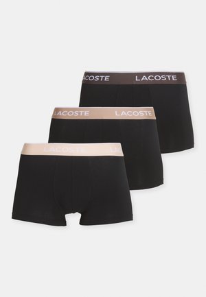 Trys juostinių trumpikių poros juodos ir šviesiai rudos spalvos, su elastingomis juostelėmis, ant kurių yra balta "LACOSTE" logotipas, pagaminti iš lygaus medvilnės audinio.