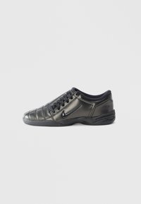 Black low-top Nike sneaker with laces, stitched detailing, and a textured sole against a plain white background.