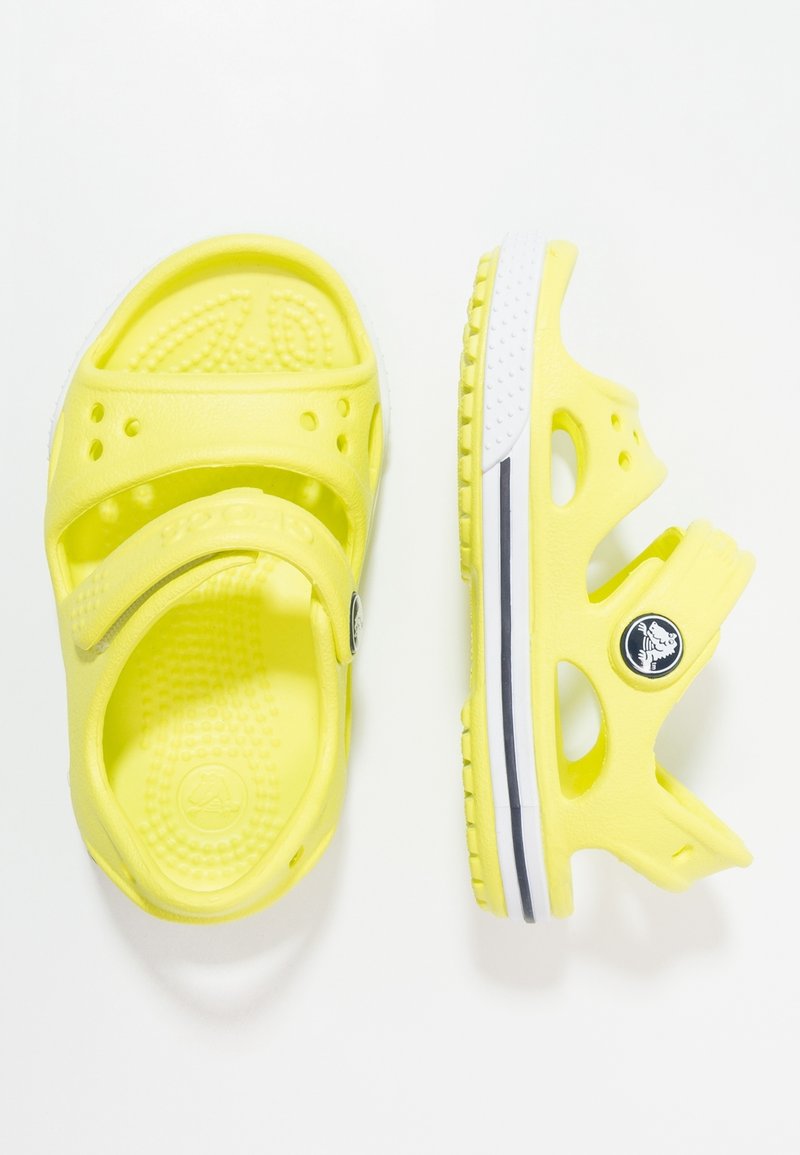 Sandales jaunes avec trous de ventilation et bride ajustable, semelle texturée, et logo noir et blanc sur la bride du talon, vues de dessus et de côté.