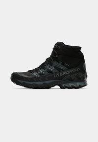 Botas de caminhada em preto com cano alto, parte superior texturizada, biqueira reforçada e sola robusta. Apresenta um design de atacadores e uma marcação na lateral.