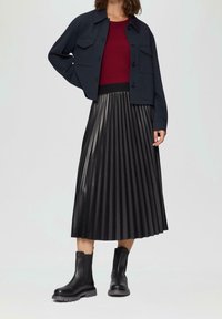 Falda midi negra con plisados combinada con una chaqueta corta azul oscura y un suéter burdeos de canalé. Botines negros completan el conjunto.