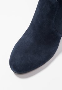 Marinblå mockaskor med spetsig tå och slät yta; har en sömlös design och lätt böjd topp. Ingen synlig hårdvara.